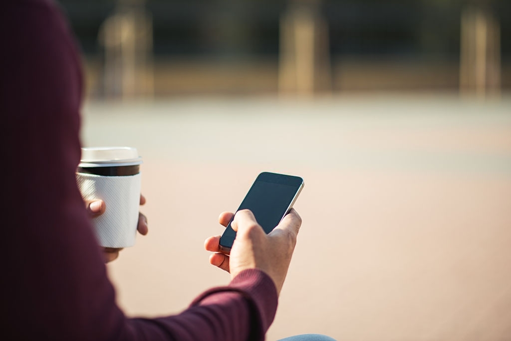 Man using a mobile phone and carrying coffee.